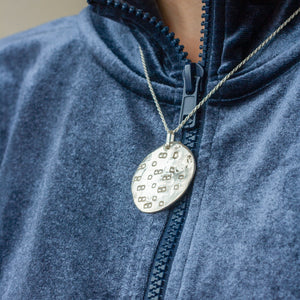 PARAGON II ROUND SILVER PENDANT WITH SQUARE PATTERN ON CHAIN BY MARGO ORLOVIK ON MODEL