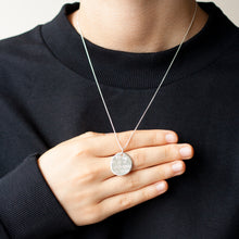 Load image into Gallery viewer, PARAGON IV SMALL ROUNDISH SILVER PENDANT WITH SQUARE PATTERN ON CHAIN BY MARGO ORLOVIK ON A MODEL&#39;S HAND
